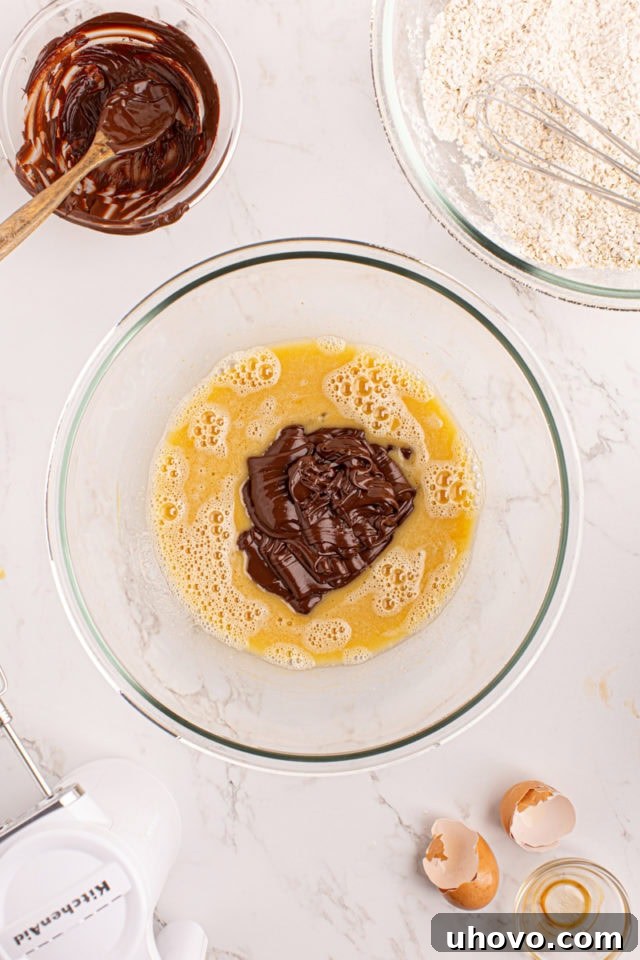Overhead view of melted semisweet chocolate being poured into a bowl of wet cookie ingredients, ready to be mixed.