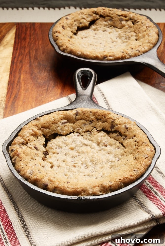 Two mini cast iron skillets holding warm, gooey chocolate chip cookies, ready for a scoop of ice cream.
