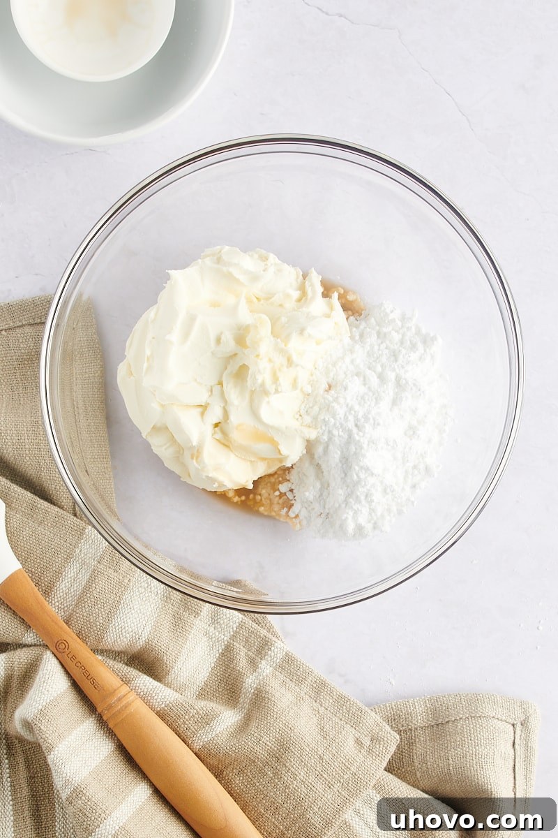 Ingredients for mascarpone frosting (mascarpone, confectioners' sugar, vanilla) in a mixing bowl, being beaten.