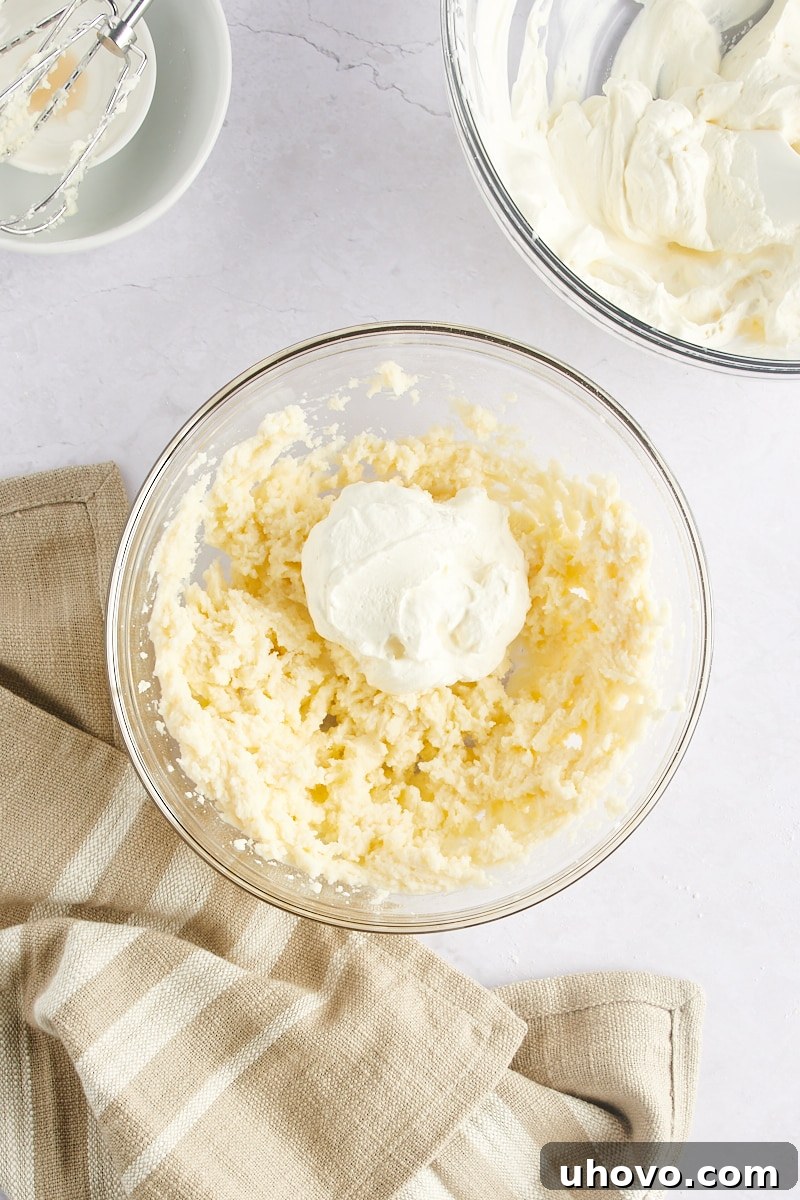 A quarter of whipped cream added to a bowl of beaten mascarpone mixture.