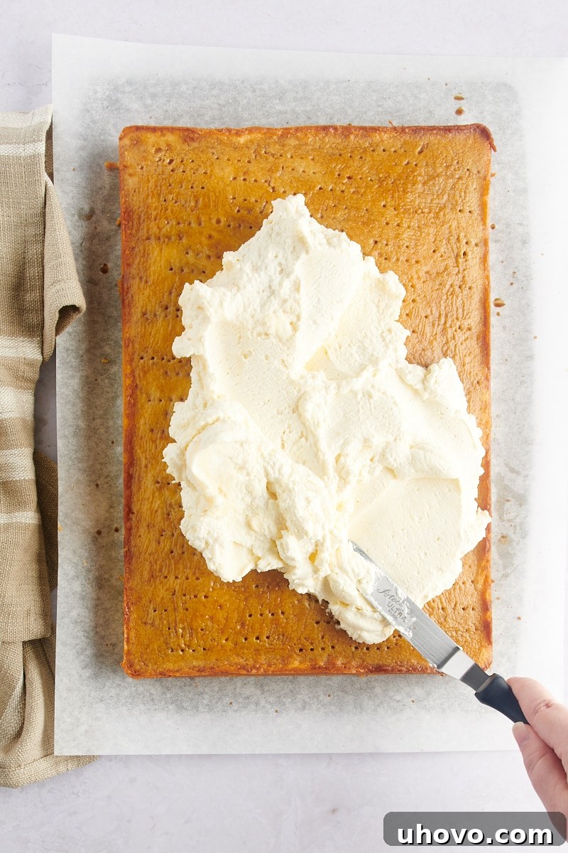 Spreading mascarpone frosting onto a coffee-soaked vanilla cake with holes.