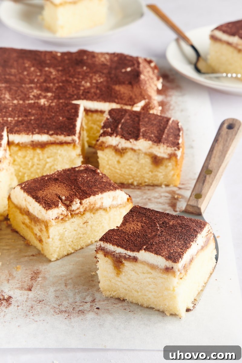 Serving tiramisu cake slices directly from the baking pan using parchment paper.