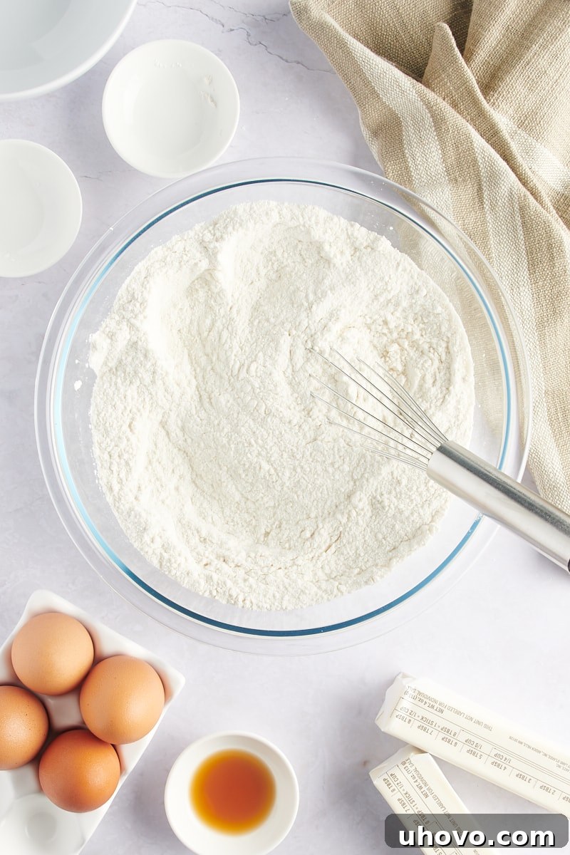 Overhead view of dry cake ingredients (flour, sugar, baking powder, salt) in a mixing bowl with a whisk.