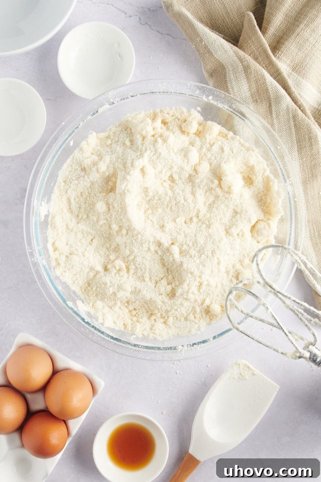 Overhead view of dry cake ingredients and softened butter in a mixing bowl, showing a sandy texture.