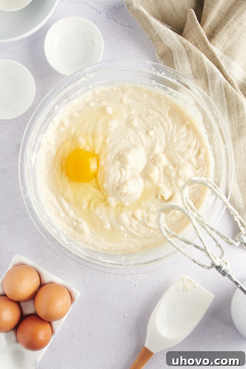Overhead view of an egg cracked into a bowl of cake batter, mid-mixing.
