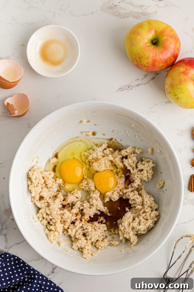 Overhead view of eggs and vanilla extract being added to the creamed butter and sugar mixture in a large mixing bowl