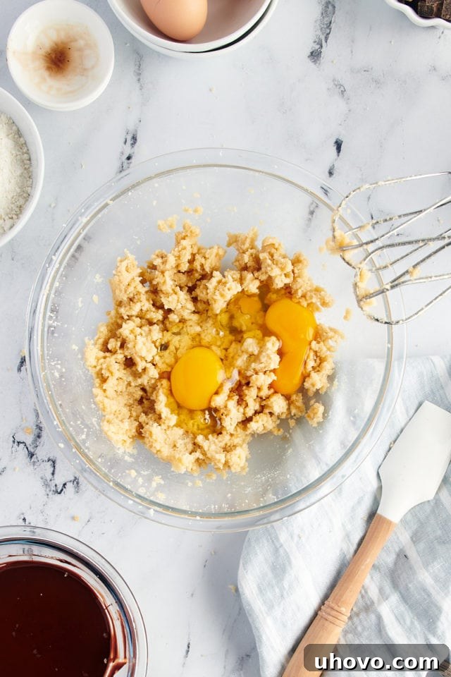 Overhead view of eggs cracked into bowl with creamed butter and sugar