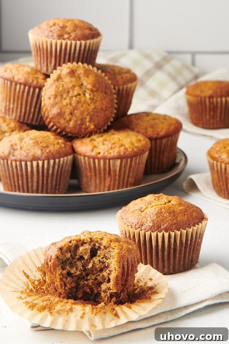 A beautifully textured, sliced banana nut muffin, revealing its moist interior and bits of banana and nuts, surrounded by other whole muffins.