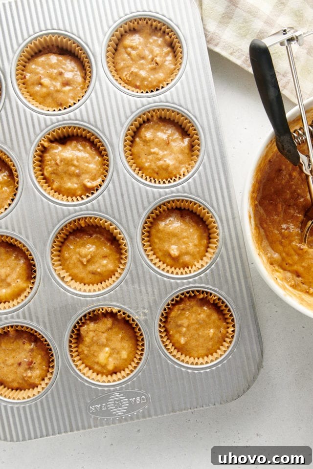Overhead view of golden-brown banana nut muffin batter perfectly portioned into a 12-cup muffin pan, filling each cup about three-quarters full.