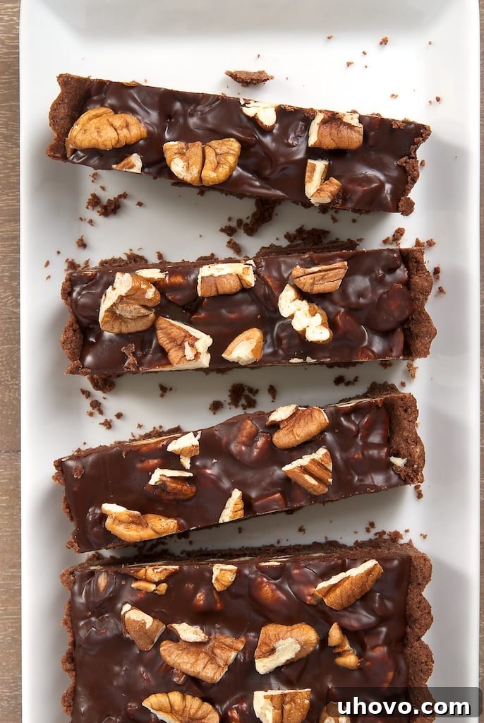 Overhead view of several slices of a rich Chocolate Pecan Tart arranged on a long white serving tray, showcasing the dark chocolate and crunchy pecan topping.