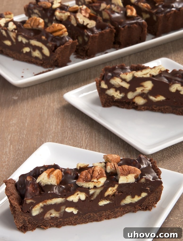 A perfectly sliced piece of Chocolate Pecan Tart resting on a white plate, revealing the layers of chocolate crust, ganache, and pecan filling.