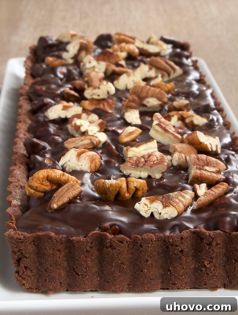 A whole Chocolate-Pecan Tart beautifully presented on a long white serving tray, ready to be sliced and enjoyed.