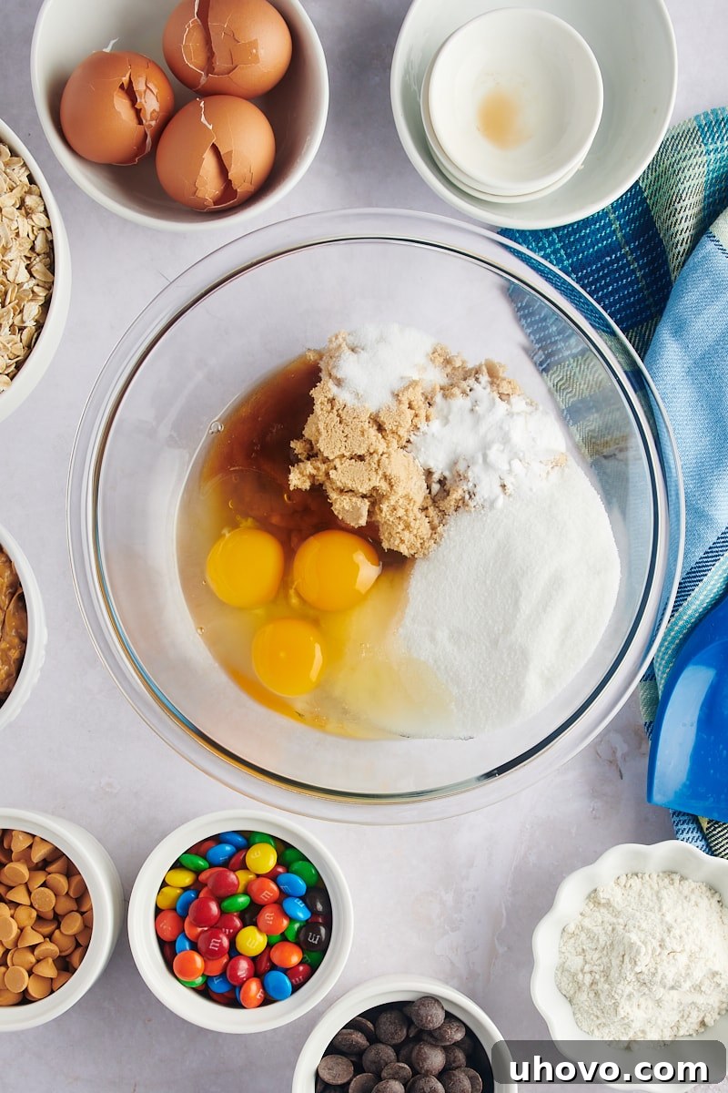 Overhead view of sugar and eggs being combined in a large mixing bowl, the first step in making monster cookies.