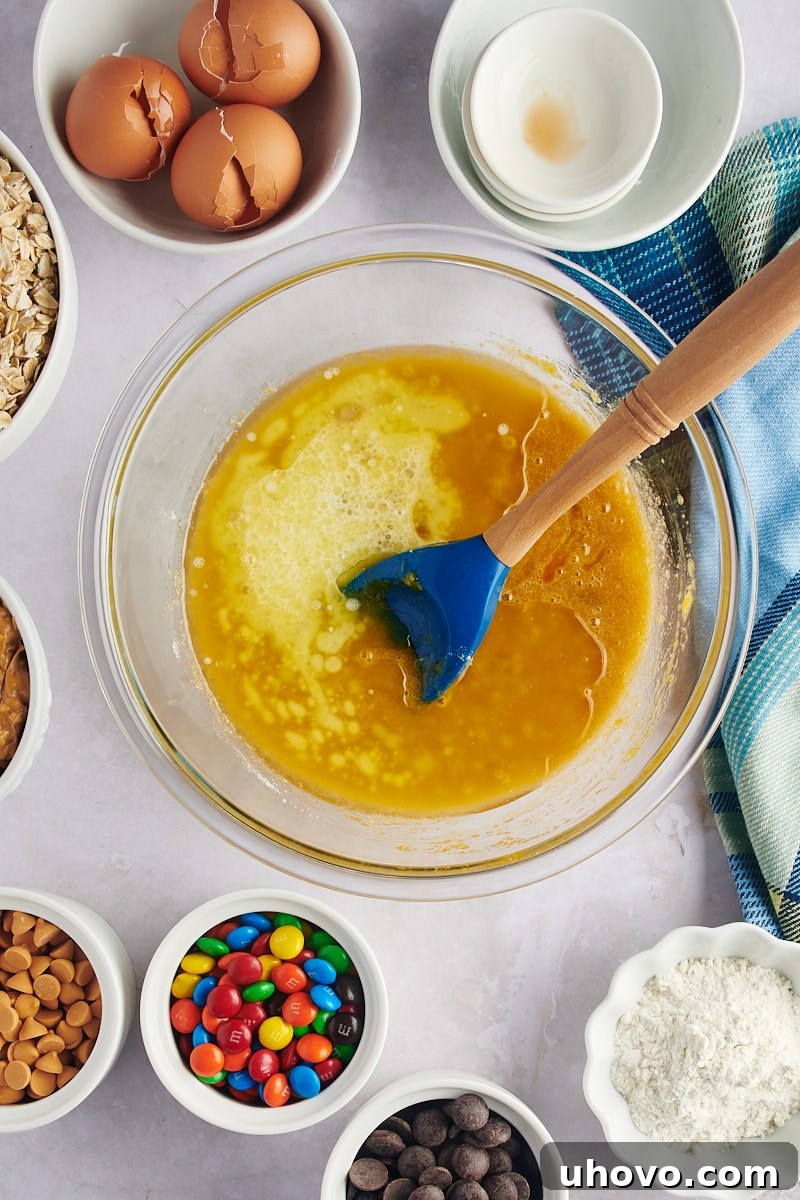 A hand stirring the wet ingredients in a mixing bowl for monster cookies, showcasing the consistency of the mixture.