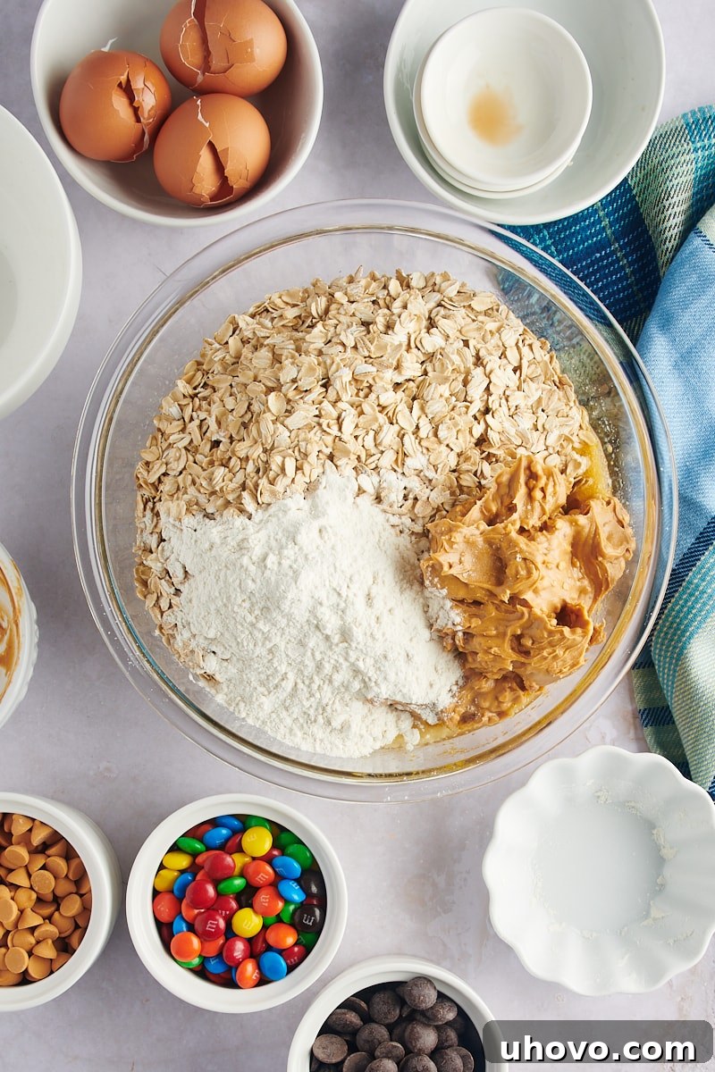 Flour, oats, and peanut butter being added to a bowl of monster cookie dough, showing the thickening texture.