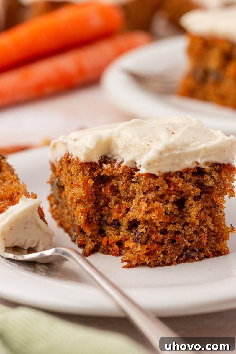A perfectly sliced carrot sheet cake topped with a generous swirl of browned butter cream cheese frosting, ready to be enjoyed.