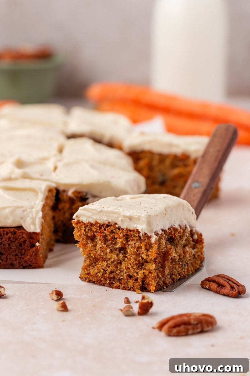 A beautiful slice of carrot sheet cake adorned with browned butter cream cheese frosting sits beside the remaining larger cake, showcasing its perfect texture.