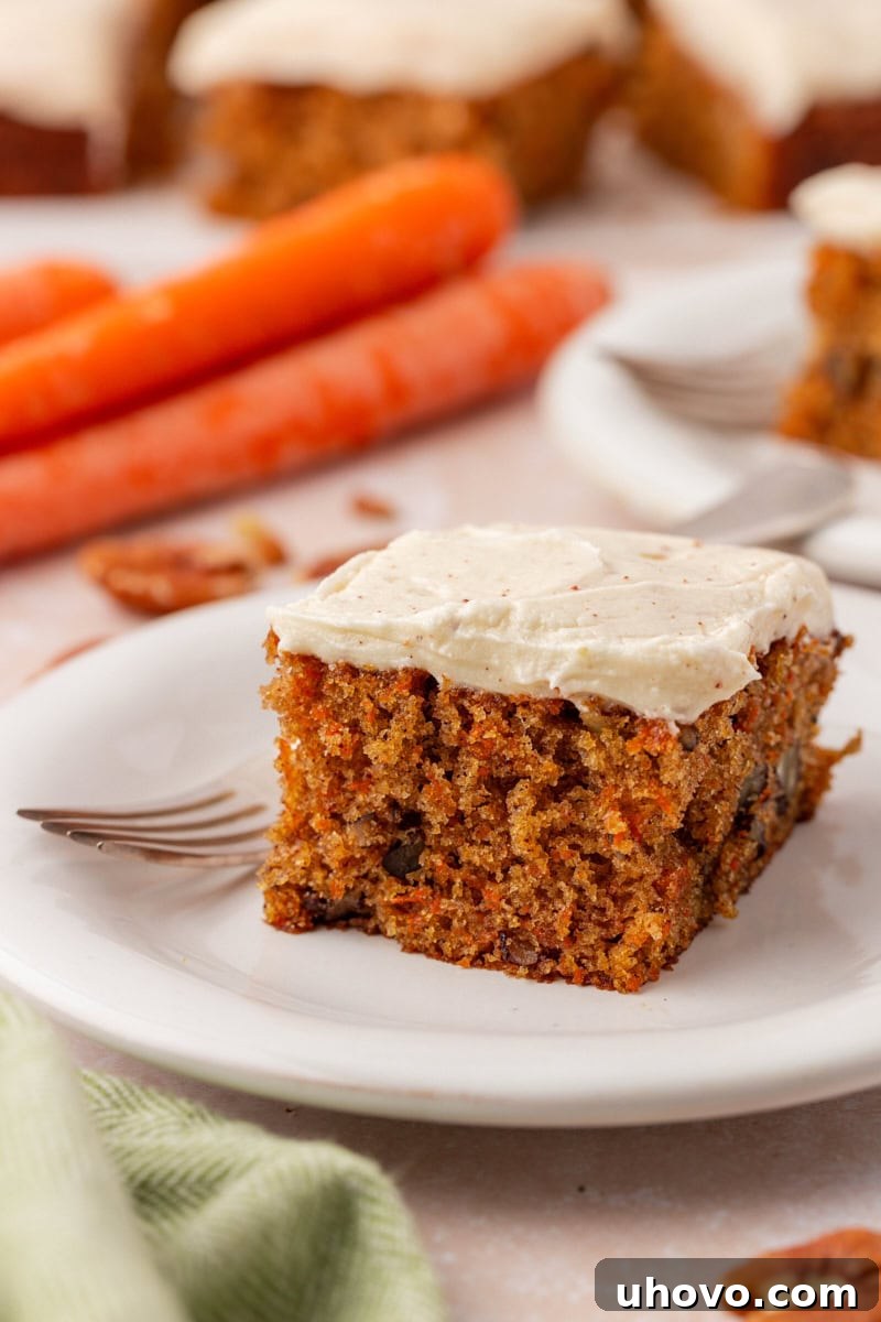 A single, delectable slice of carrot sheet cake, generously topped with creamy browned butter cream cheese frosting, presented beautifully on a pristine white plate.