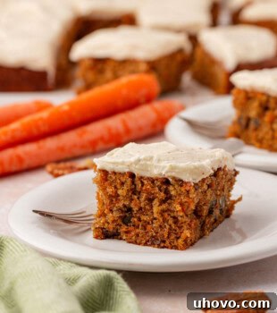 A close-up of a delightful slice of carrot sheet cake, exquisitely frosted with browned butter cream cheese frosting, on a white plate with the full cake visible in the background.
