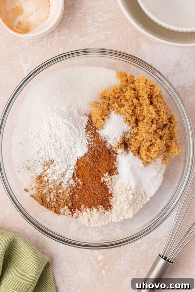 An overhead view of various dry ingredients like flour, sugars, baking powder, baking soda, and a blend of spices meticulously combined in a spacious mixing bowl.