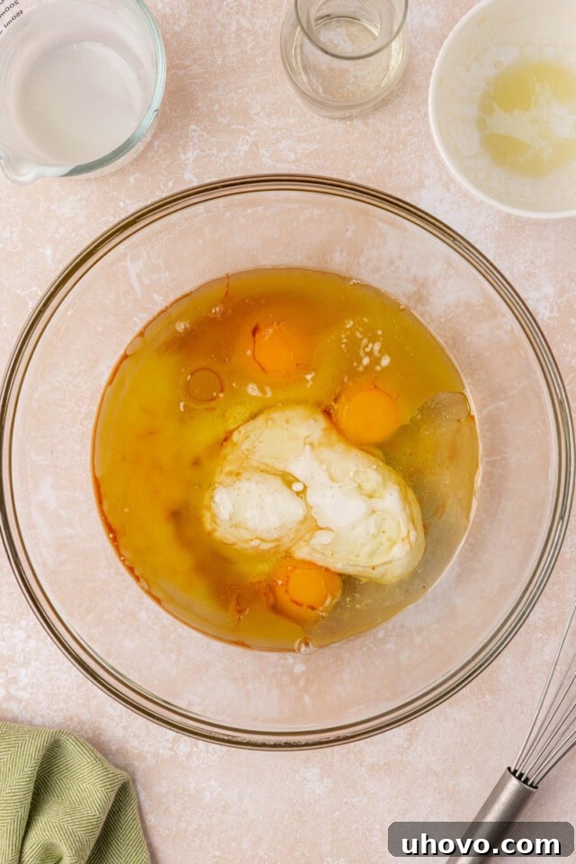 A close-up, overhead shot of a mixing bowl containing eggs, melted butter, neutral cooking oil, buttermilk, and vanilla extract, all whisked together until smooth and evenly blended.