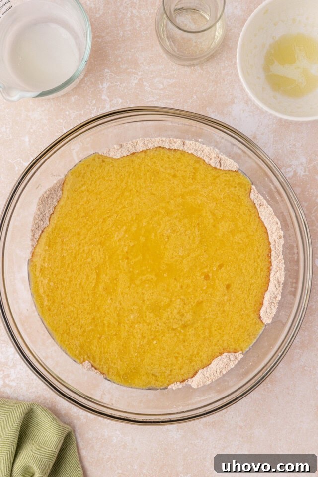 An image showing the moment wet ingredients are carefully poured into the bowl of dry ingredients for the carrot cake, ready for gentle mixing.