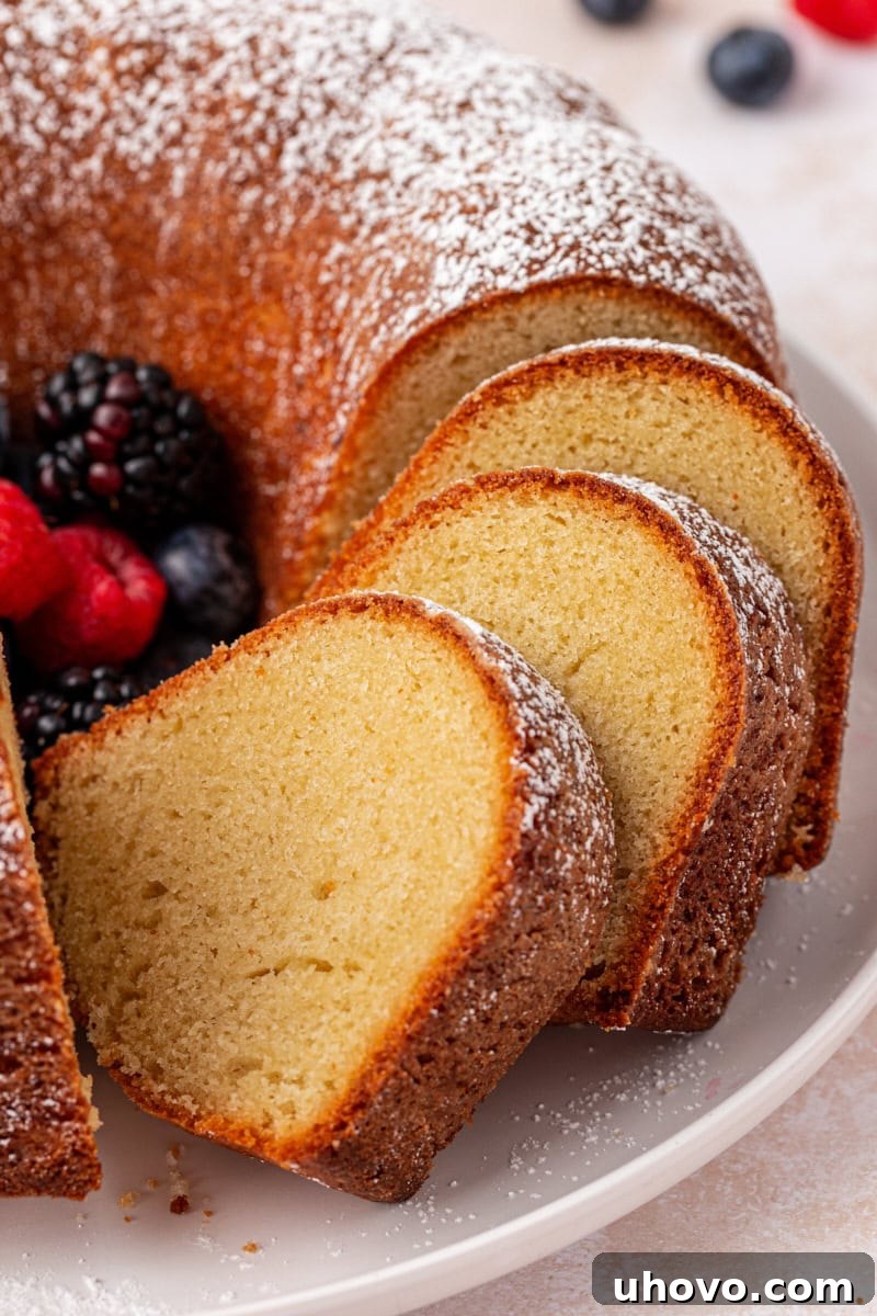 Close up of a partially sliced buttermilk pound cake topped with powdered sugar, showcasing its tender crumb and golden crust.