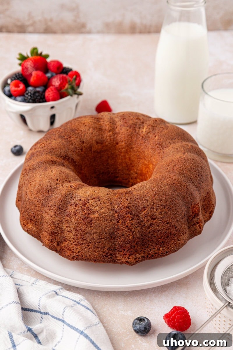 A whole buttermilk pound cake, elegantly simple, presented on a white cake plate.