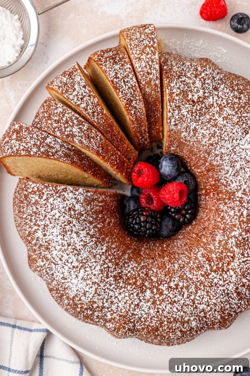 A partially sliced buttermilk pound cake, dusted with powdered sugar and generously served with fresh mixed berries.