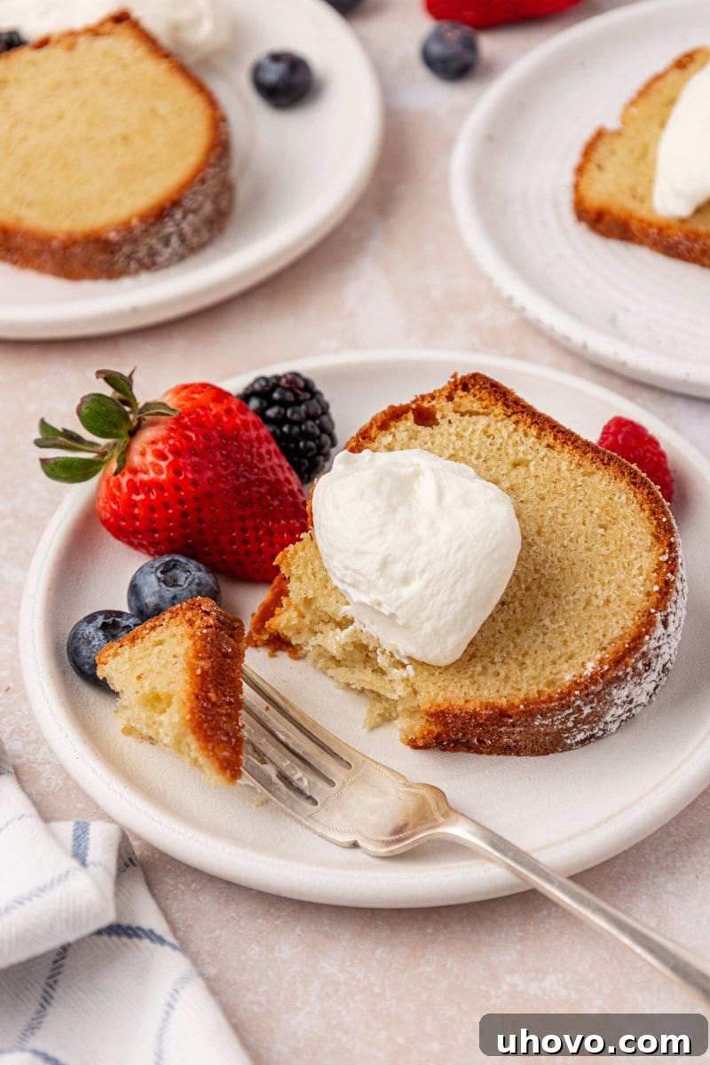A perfectly portioned slice of buttermilk pound cake, generously topped with sweetened whipped cream and a vibrant medley of fresh berries, ready to be enjoyed.