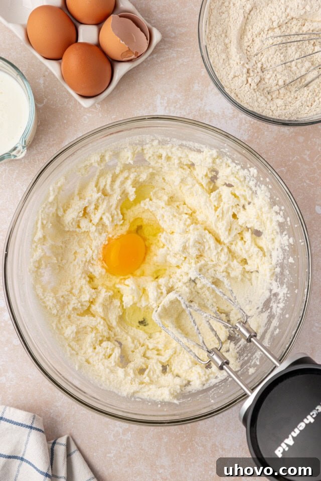 Overhead view of an egg being added to a mixing bowl containing creamed butter and sugar, indicating the next step in making pound cake.