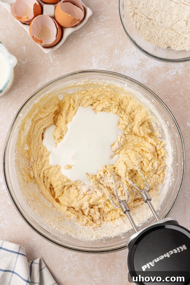 Overhead view of buttermilk being poured into the pound cake batter, demonstrating the alternating addition technique.