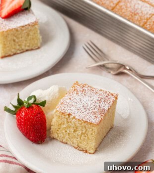 A slice of hot milk cake, elegantly topped with powdered sugar and served alongside fresh whipped cream and a juicy strawberry, inviting a taste of its delicate crumb.