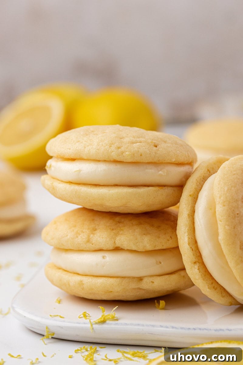 A stack of two soft lemon whoopie pies with a bright yellow lemon cream cheese filling, garnished with lemon zest.