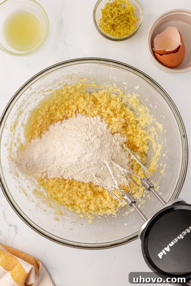Dry ingredients, including flour, baking powder, baking soda, and salt, are being added to the lemon whoopie pie batter in a mixing bowl.