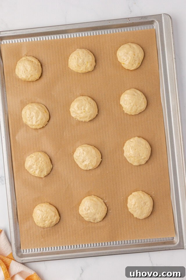 Lemon whoopie pie batter neatly portioned onto a parchment-lined baking sheet, ready to be baked in the oven, showing even spacing.