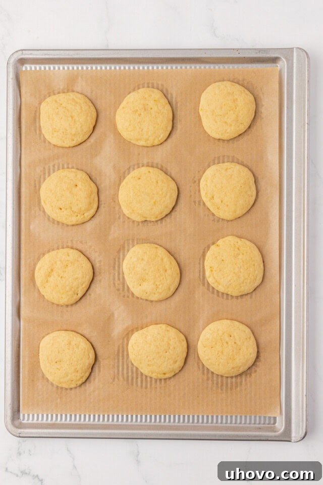 Overhead view of freshly baked, golden-brown, soft lemon whoopie pie cookies cooling on a wire rack, exhibiting a slight domed top.