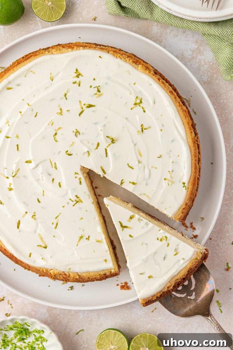 Creamy Key Lime Cheesecake Recipe: Zesty No-Bake Dessert 8 partially sliced Key lime cheesecake with sour cream topping and a sprinkle of lime zest