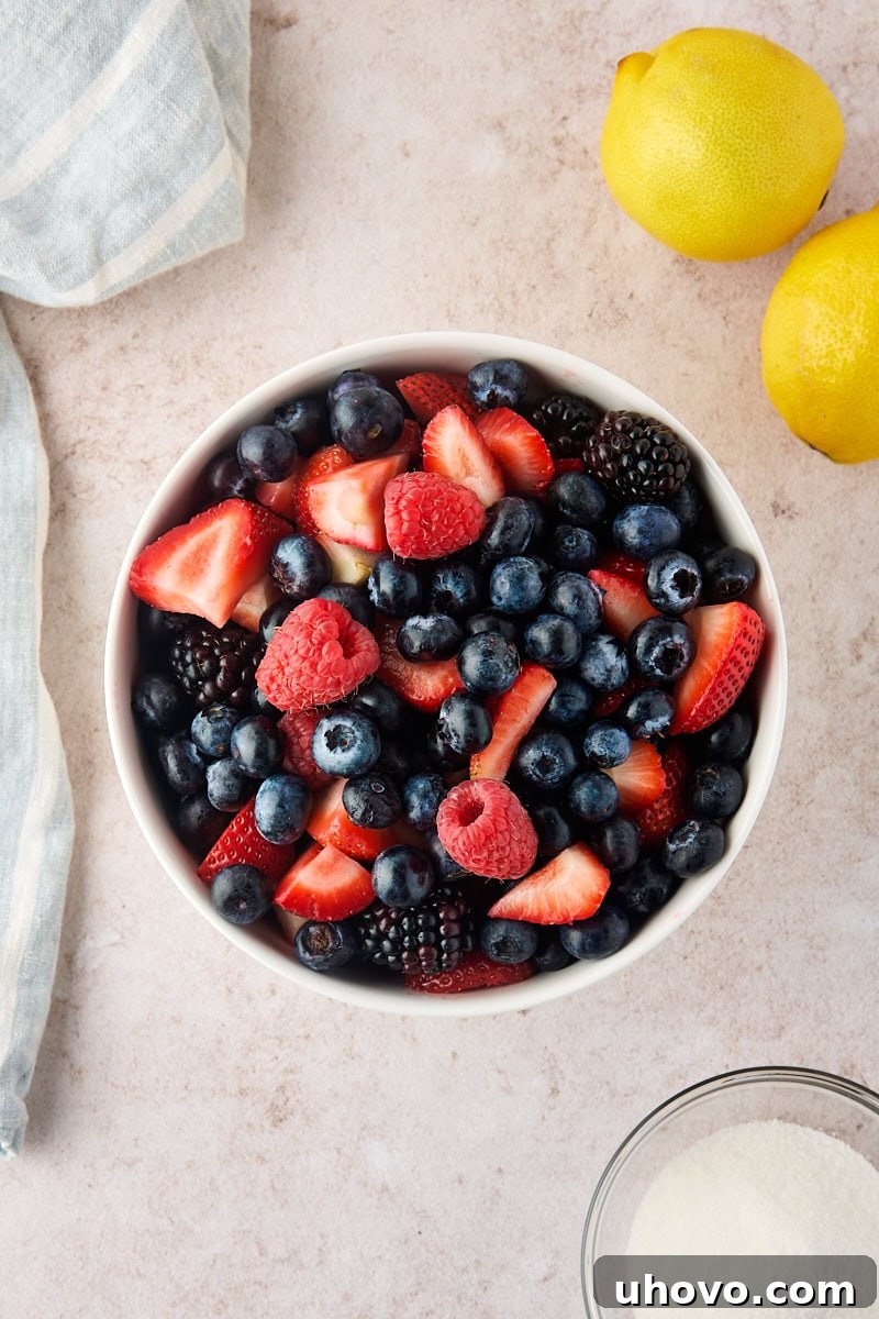 Macerated Berries Recipe: Sweetened Berry Topping for Desserts 3 fresh mixed berries in a bowl, with lemons and a bowl of sugar alongside