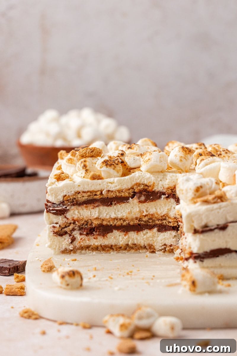 No-Bake S'mores Icebox Cake 10 partially sliced s'mores icebox cake with layers of marshmallow filling, chocolate ganache, and graham crackers