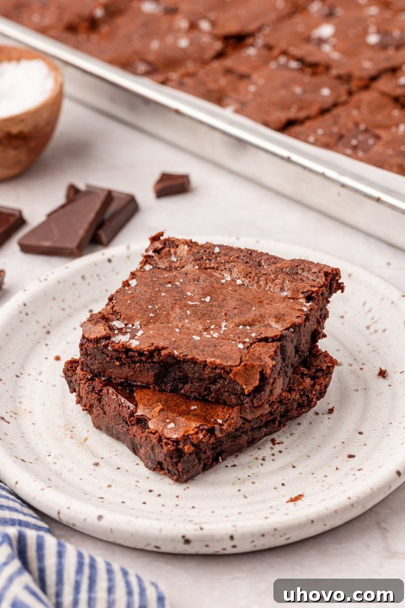 two stacked brownies on a plate with remaining brownies in a sheet pan in the background