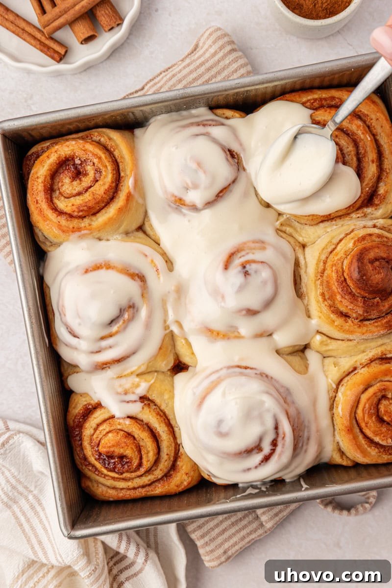 Overnight Cinnamon Roll Recipe for Fluffy Morning Pastry 10 cream cheese frosting being spread over warm cinnamon rolls in a square baking pan