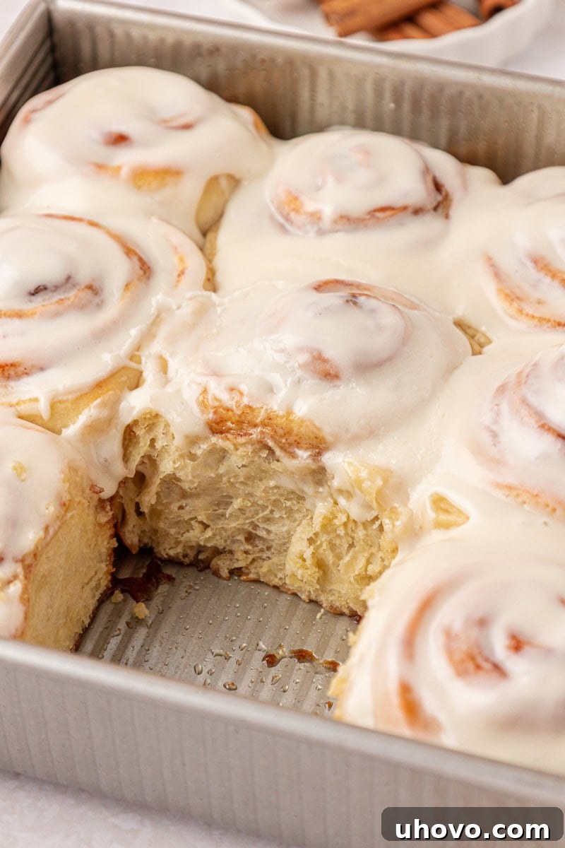 Overnight Cinnamon Roll Recipe for Fluffy Morning Pastry 11 frosted cinnamon rolls in a metal baking pan with one roll missing