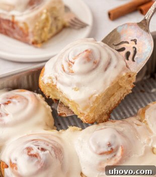 Overnight Cinnamon Roll Recipe for Fluffy Morning Pastry 13 a cinnamon roll on a cake server being lifted away from the remaining rolls in a square baking pan