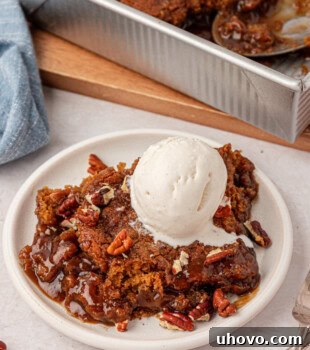 butterscotch pudding cake on a white plate with a scoop of vanilla ice cream and toasted pecans