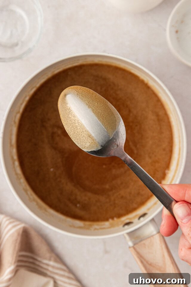 thick brown sugar caramel coating a spoon above a saucepan while making pecan pie cheesecake bar topping