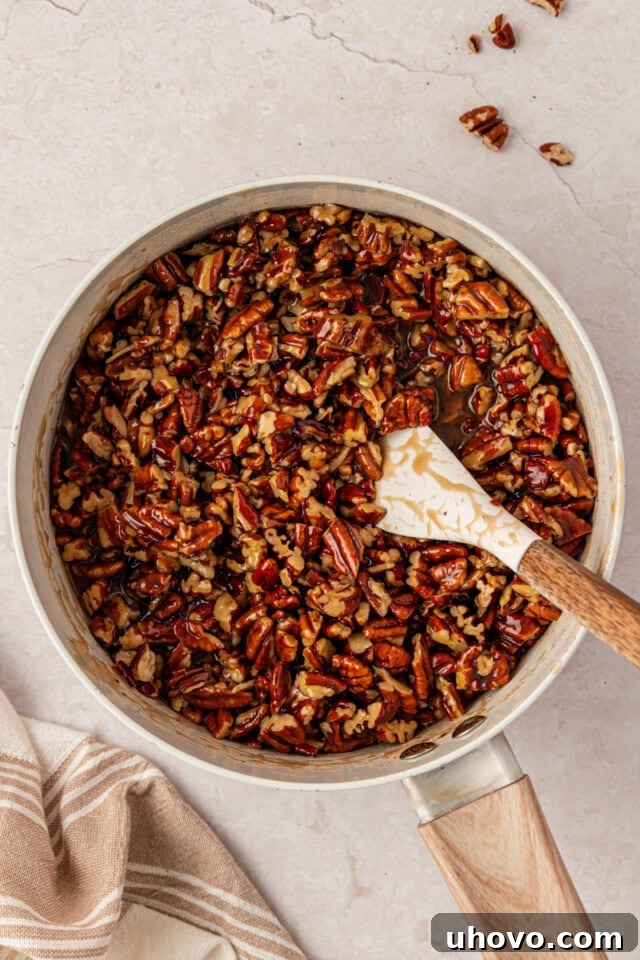 chopped pecans coated in glossy brown sugar caramel in a saucepan, with a spatula resting in the mixture