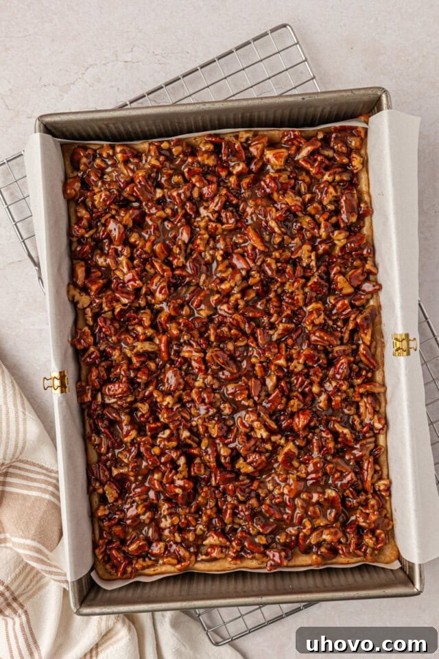 gooey pecan pie topping spread over cheesecake bars in a 9x13 pan