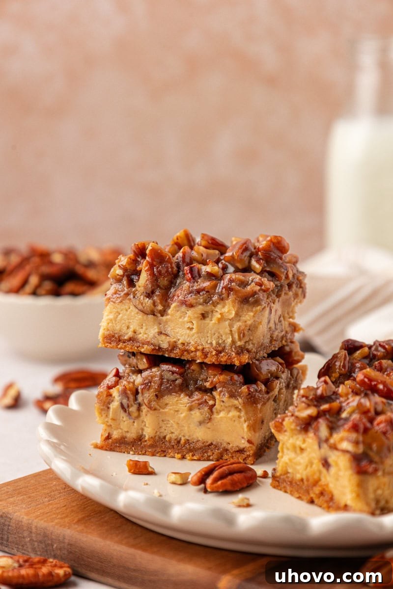 two stacked pecan pie cheesecake bars with layers of graham cracker crust, brown sugar cheesecake, and gooey pecan pie topping